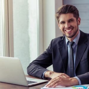 Smiling businessman in suit working on laptop at office desk.